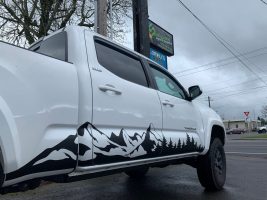 Side of white truck with black decal of mountains and trees